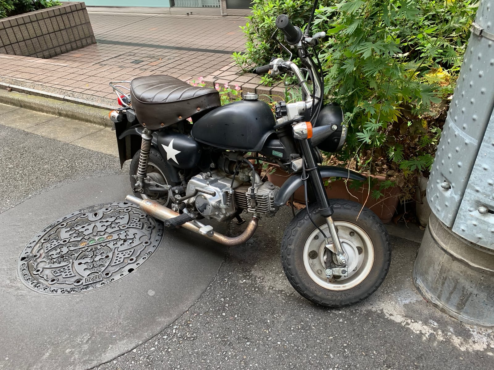A matte black mini motorcycle with a white star on its side panel, parked over an ornate manhole cover