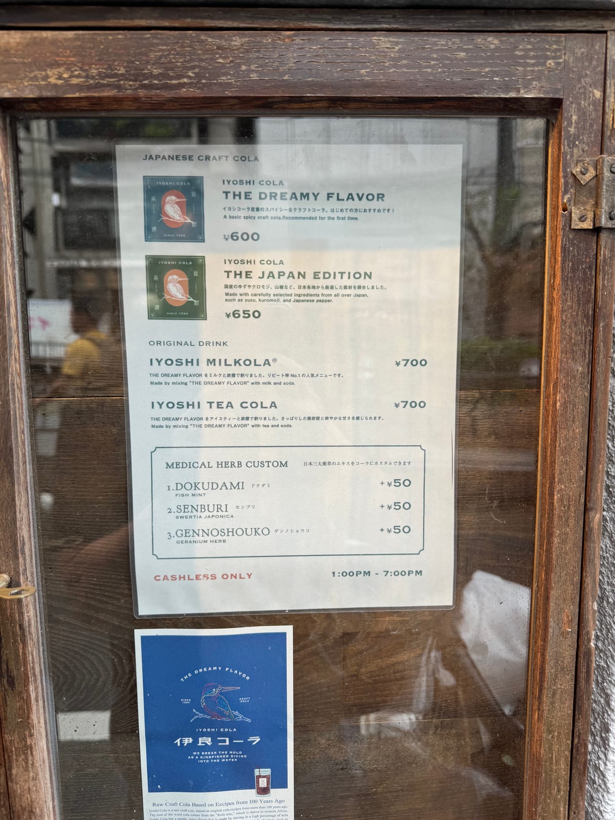 The Iyoshi Cola menu board behind glass in a wooden frame: The Dreamy Flavor, The Japan Edition, Milkola, Tea Cola, and the medical herb custom