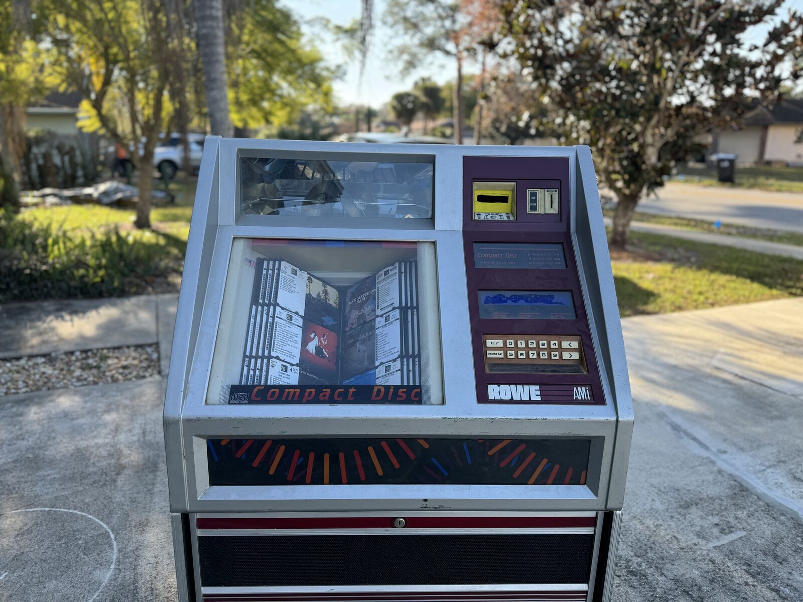 Closer view of the jukebox top: discs visible through the carousel window, album title cards behind glass, and the Rowe AMI keypad
