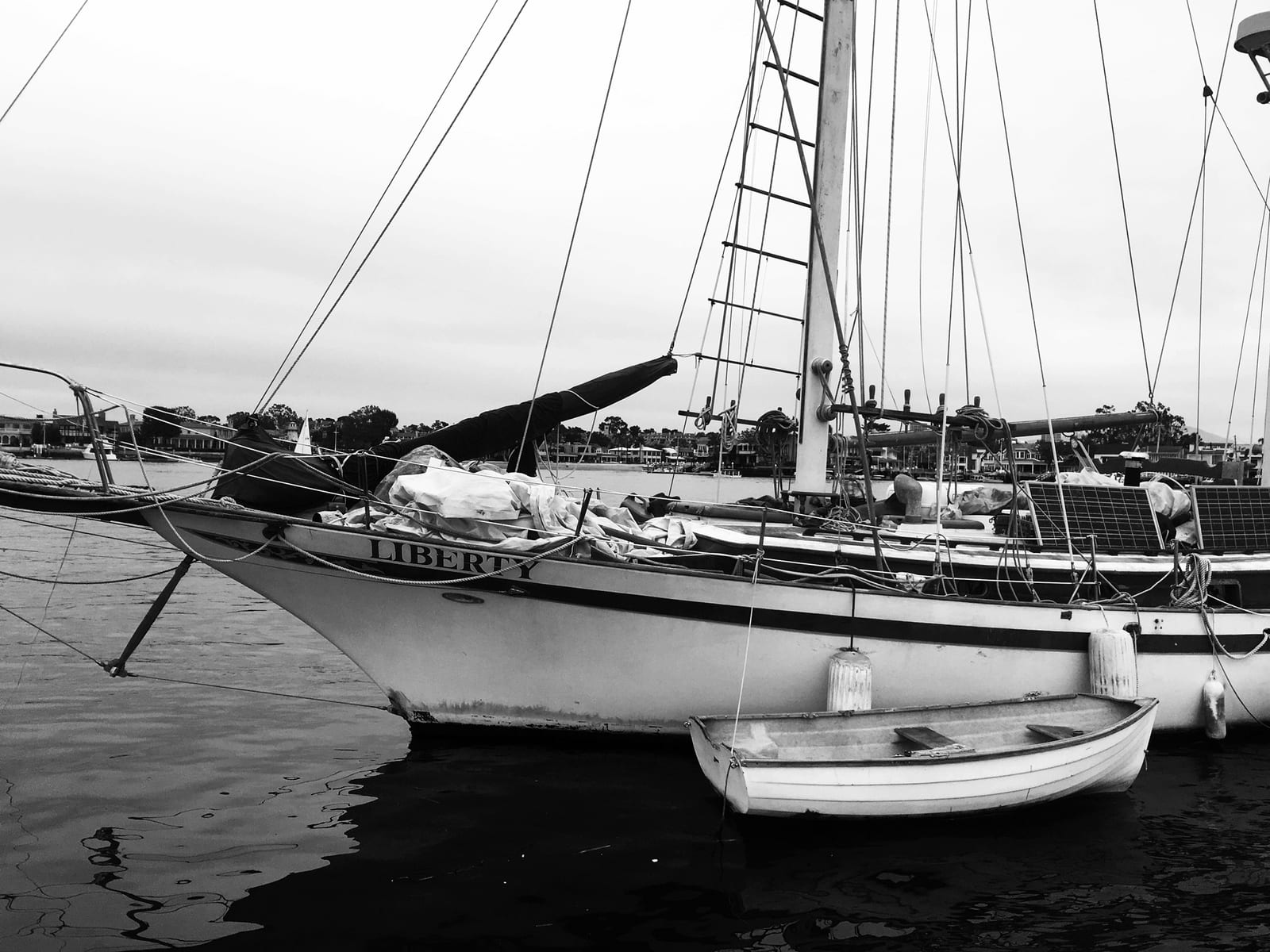 The ketch Liberty at anchor with a white dinghy tied alongside, sails bundled on deck and rigging against a flat sky