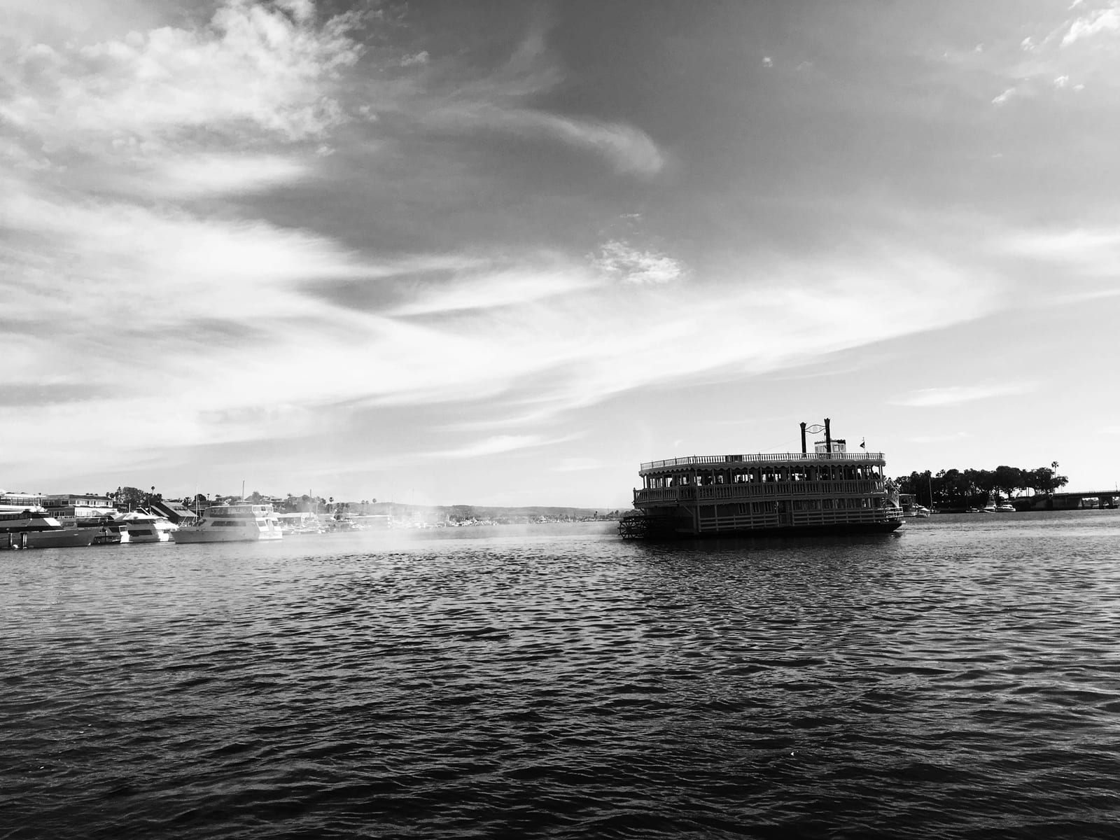A two-deck paddlewheeler crossing the harbor under a wide, streaked sky, the far shore low on the horizon